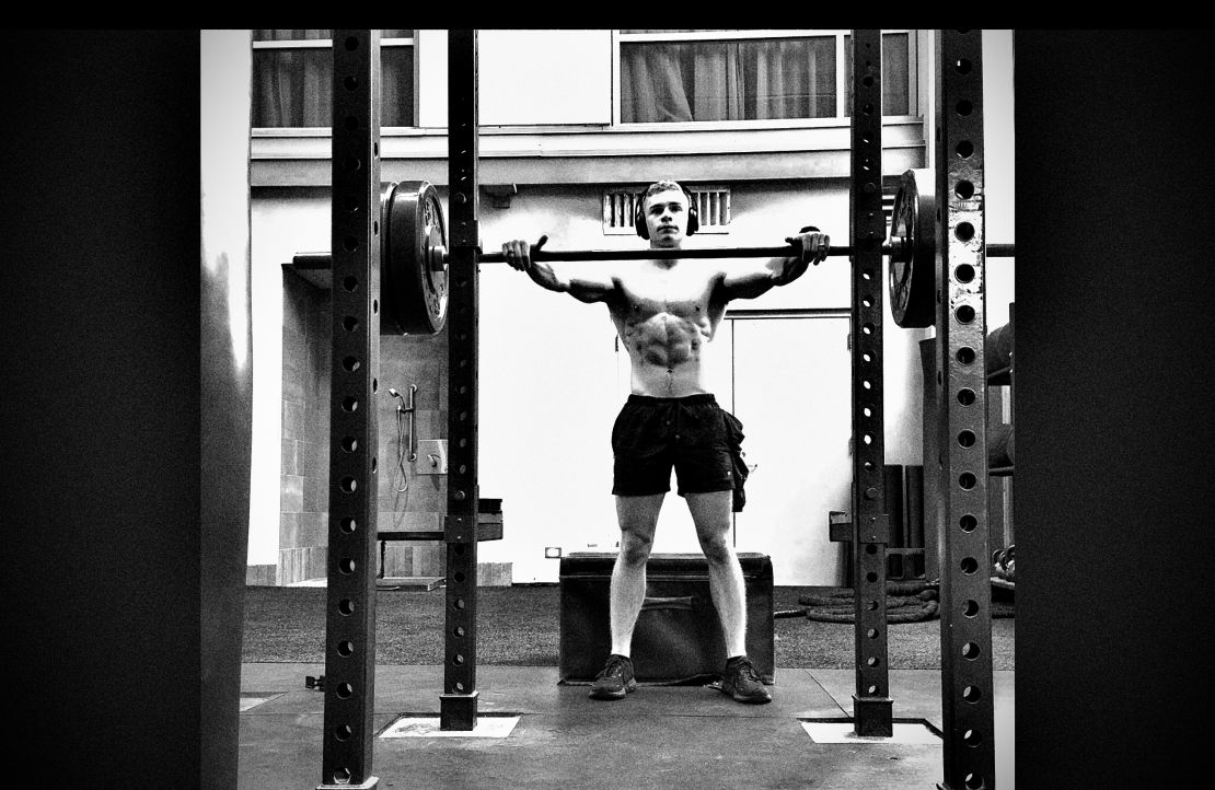 Coach performing a barbell front rack hold in a power rack